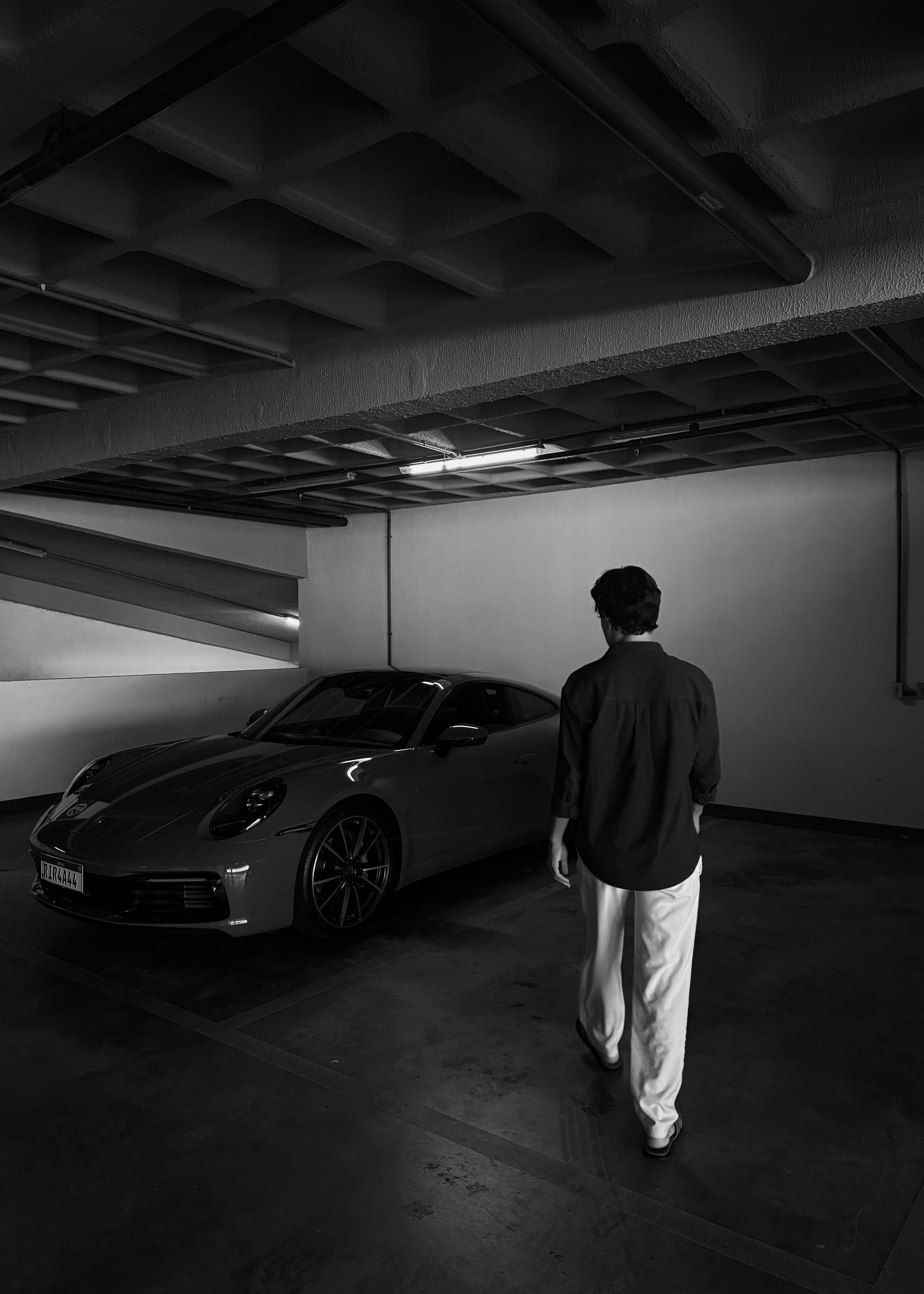 Jason Sowza, fundador da WHOFY SCALE, caminhando em direção a um Porsche 911 em uma garagem subterrânea